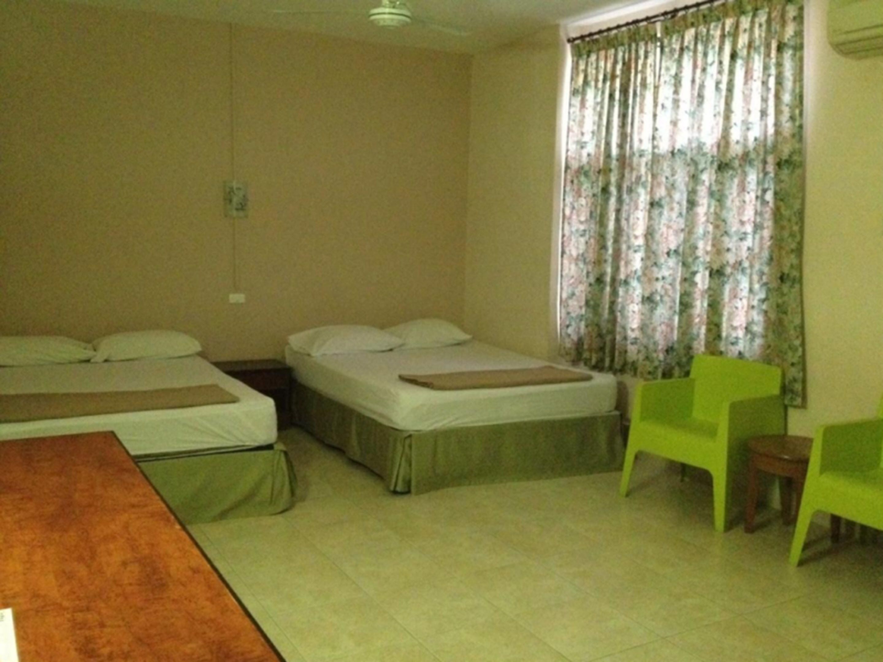 A hotel room with two beds, a wooden table, and a green chair.