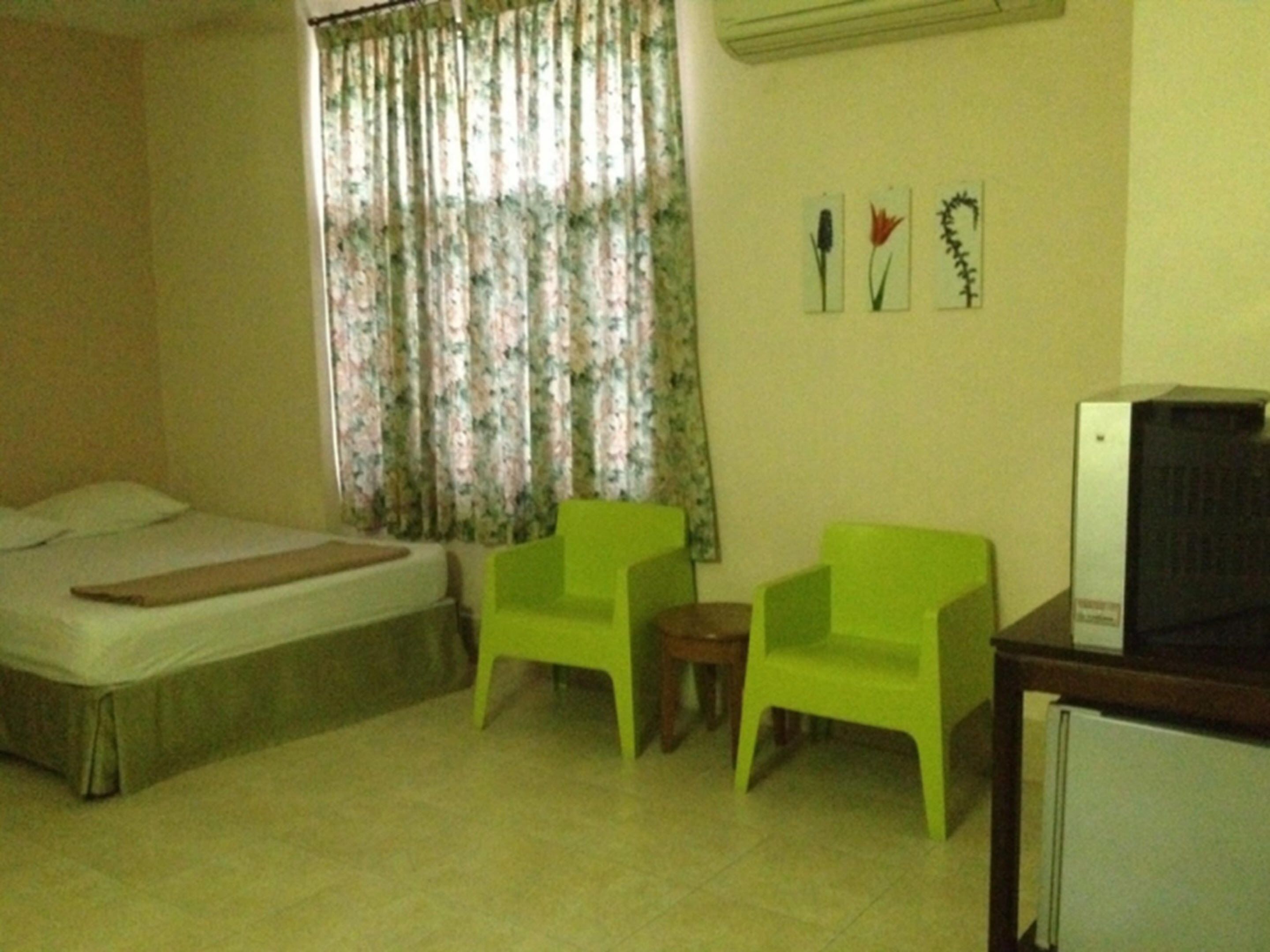 A room with a bed, two green chairs, a small table, and a TV on a stand.
