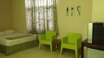 A room with a bed, two green chairs, a small table, and a TV on a stand.