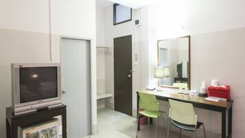 A hotel room with a television on a stand, a desk with a chair, a mirror, and a small table with toiletries.