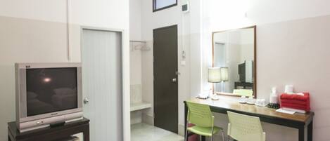 Une chambre d’hôtel équipée d’un téléviseur posé sur un meuble, d’un bureau avec une chaise, d’un miroir et d’une petite table avec des articles de toilette.