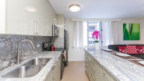 A modern kitchen with stainless steel appliances, a granite countertop, and a view to the living area. - Designer Renovated, One Bedroom, Free Parking, Washer/dryer, Walk To Beach (Honolulu)