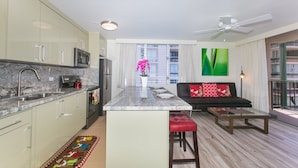 A modern kitchen with a central island, a dining area with a sofa and a coffee table, and a balcony with a view of the city. - Designer Renovated, One Bedroom, Free Parking, Washer/dryer, Walk To Beach (Honolulu)
