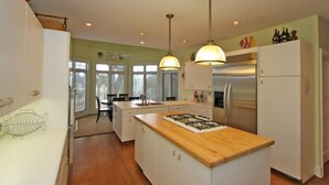 Een moderne keuken met een centraal eiland, roestvrijstalen apparatuur, hanglampen en uitzicht op de eethoek.