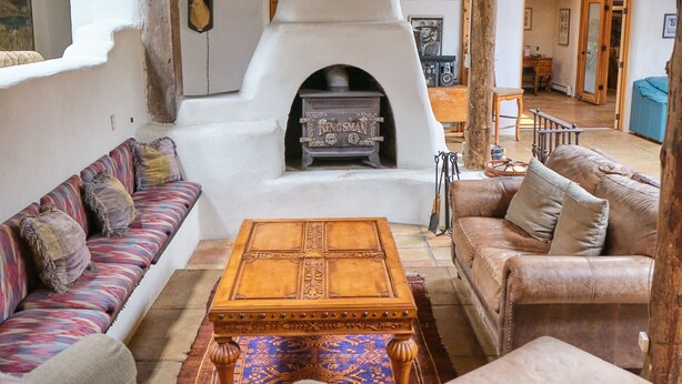 A cozy living room with a stone fireplace, wooden ceiling beams, and a sofa set. - Palace Of Miracles: Hot Tub, Lounge Spaces, +Casita, mtn views,5 courtyrds,6 FPs (El Prado)