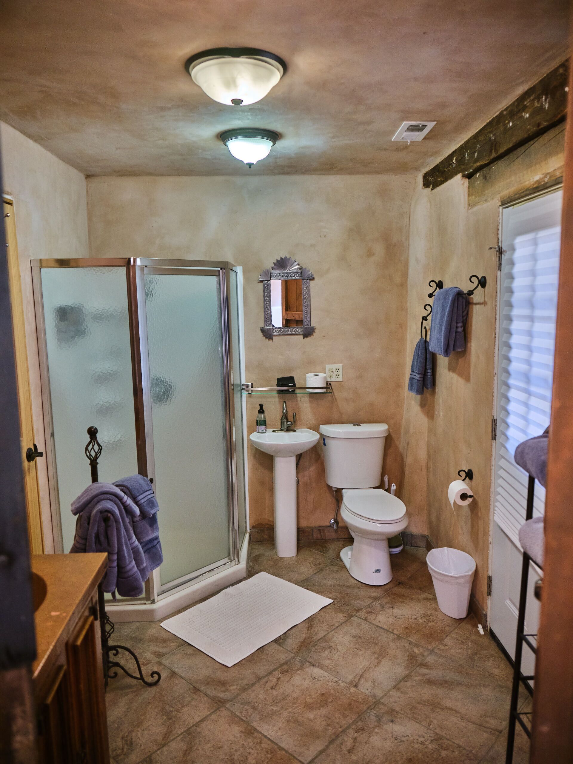 Un baño con cabina de ducha de vidrio, lavabo, inodoro y un pequeño cubo de basura.