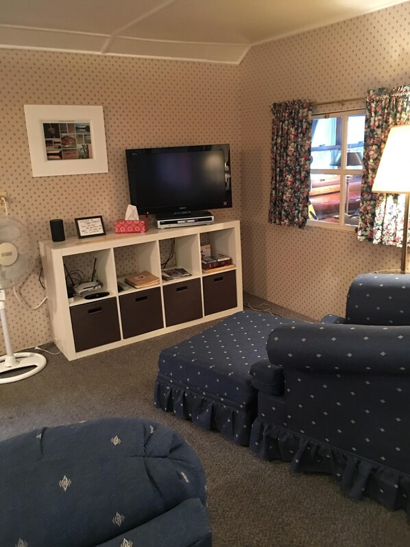 A living room with a white entertainment unit, a flat-screen TV, a fan, and patterned furniture.