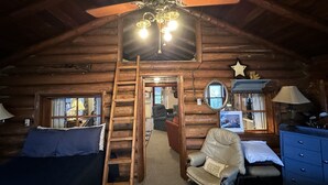 A log cabin interior with a wooden ceiling, a ceiling fan, a ladder, a chair, a dresser, and a bed. - Peaceful Vintage 1920's Lakefront Red Log Cabin (Fifty Lakes)