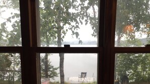 A window with a view of a lake, a chair, and a boat. - Peaceful Vintage 1920's Lakefront Red Log Cabin (Fifty Lakes)
