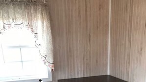 Et spisebord med fire stole, et vindue med gardin, og en trævæg.