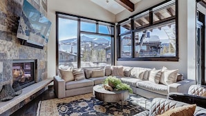 A cozy living room with a stone fireplace, large windows offering mountain views, a sectional sofa, and a coffee table with decorative items.