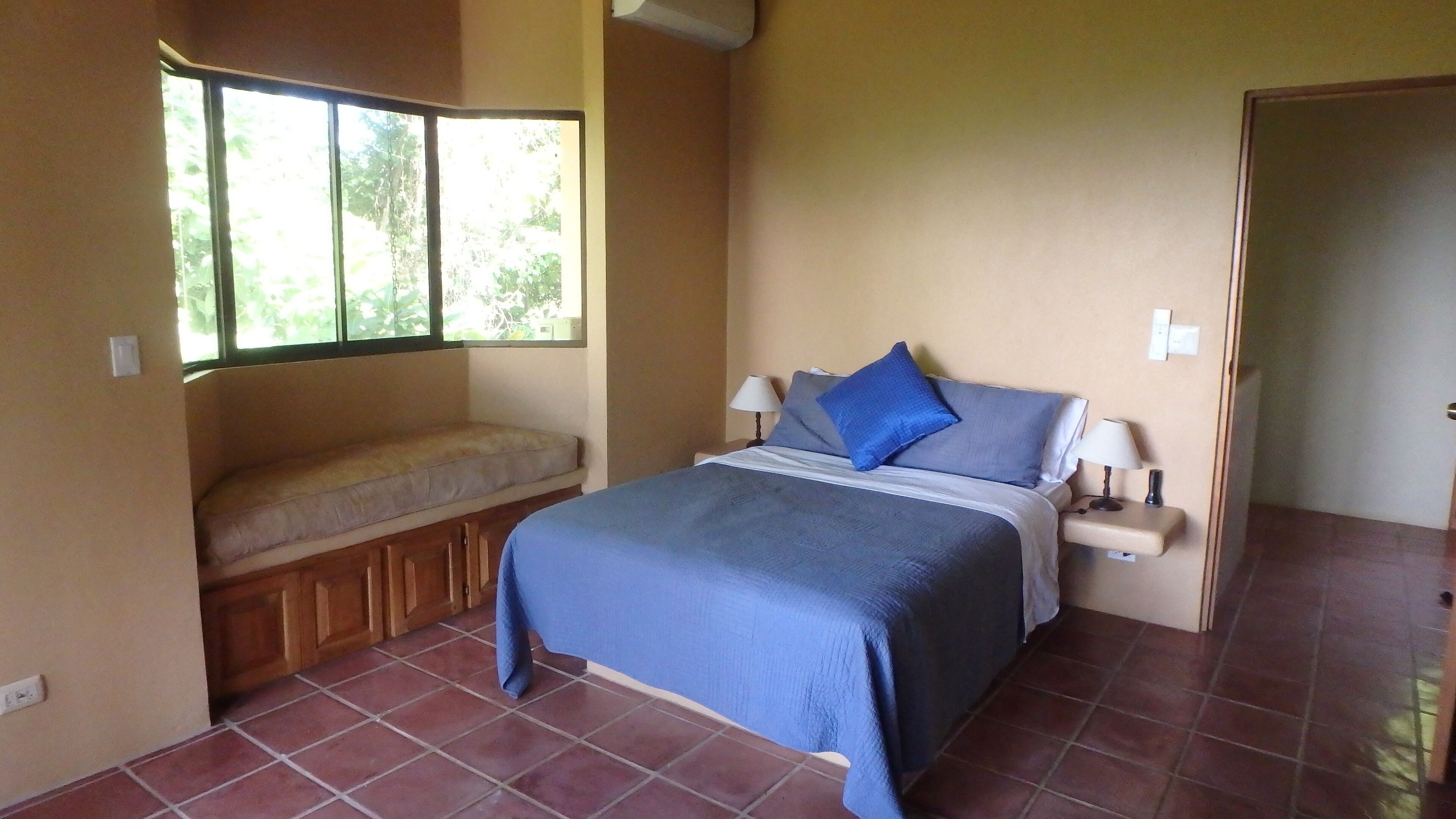 Un dormitorio con cama, lámparas de noche, un banco y una ventana.