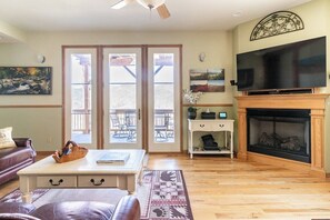 Una sala de estar con chimenea, televisor y comedor con puertas al exterior.