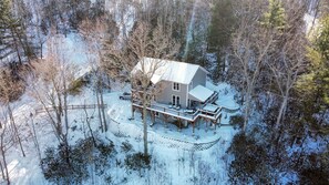 Une maison à deux étages dotée d’un porche abrité et d’une terrasse, entourée d’arbres couverts de neige.
