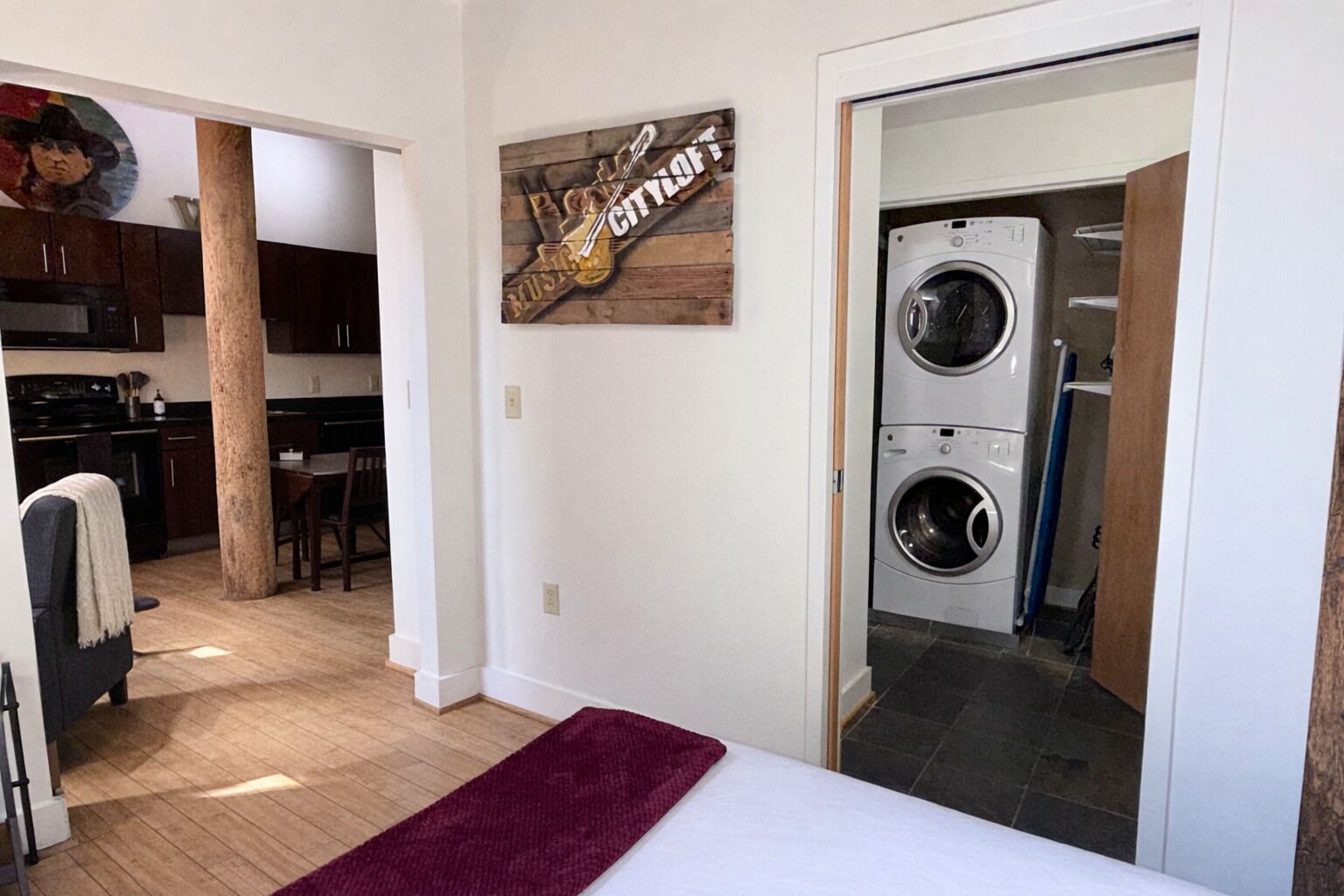 Une chambre à coucher avec un lit, un tapis rouge, un lave-linge et une enseigne en bois accrochée au mur.
