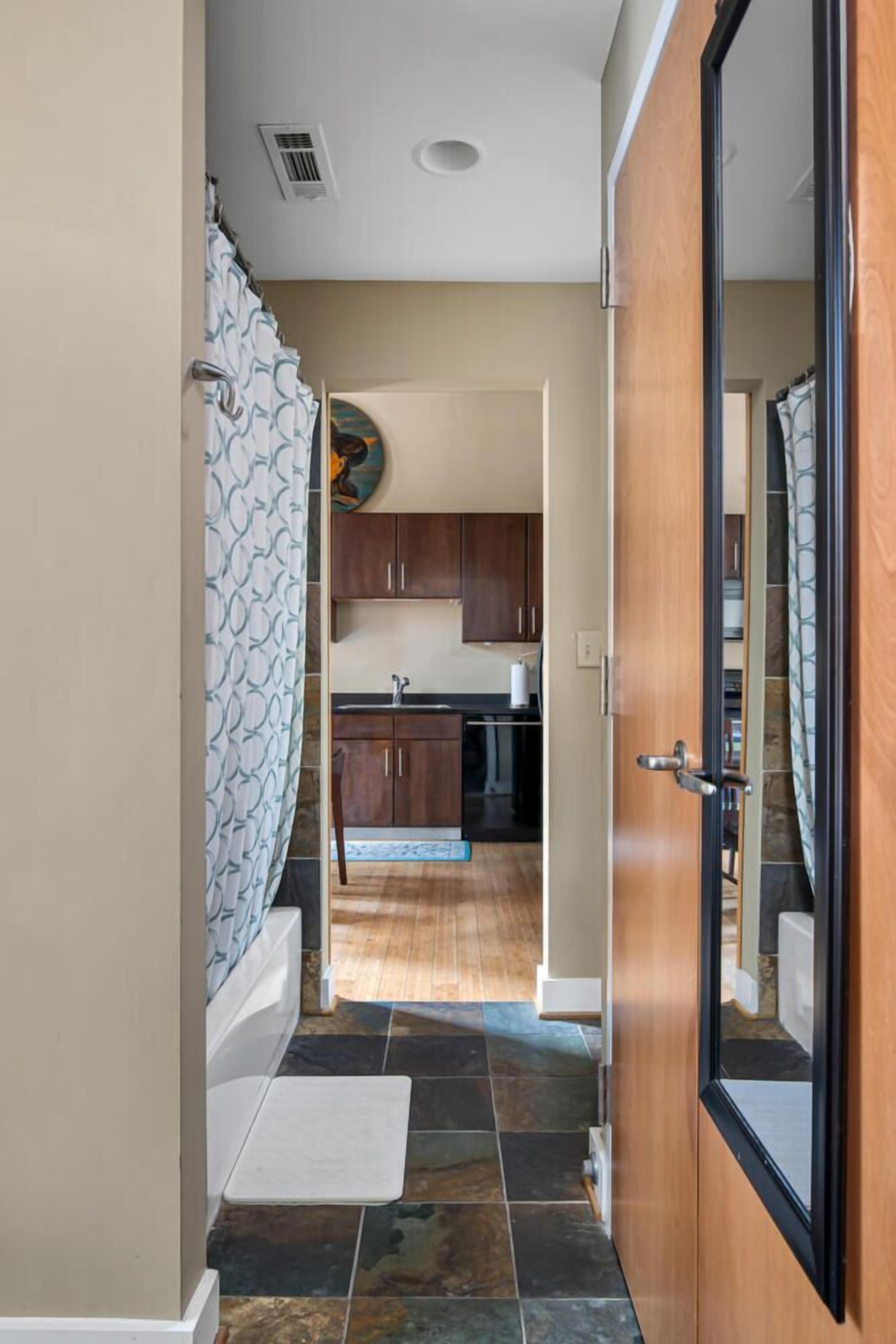 A hallway leading to a kitchen with dark tiled flooring, wooden cabinets, and a white countertop.