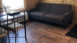 A cozy room with a wooden interior, a grey sofa, a dining table with chairs, and a large window. - 8 miles to Mount Rushmore - Sleeps 2 to 6 (Rapid City)