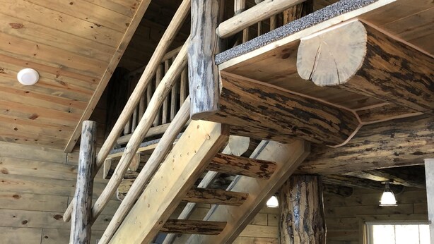 A wooden staircase with a rustic design, leading to a bed with a white cover. - 8 miles to Mount Rushmore - Sleeps 2 to 6 (Rapid City)