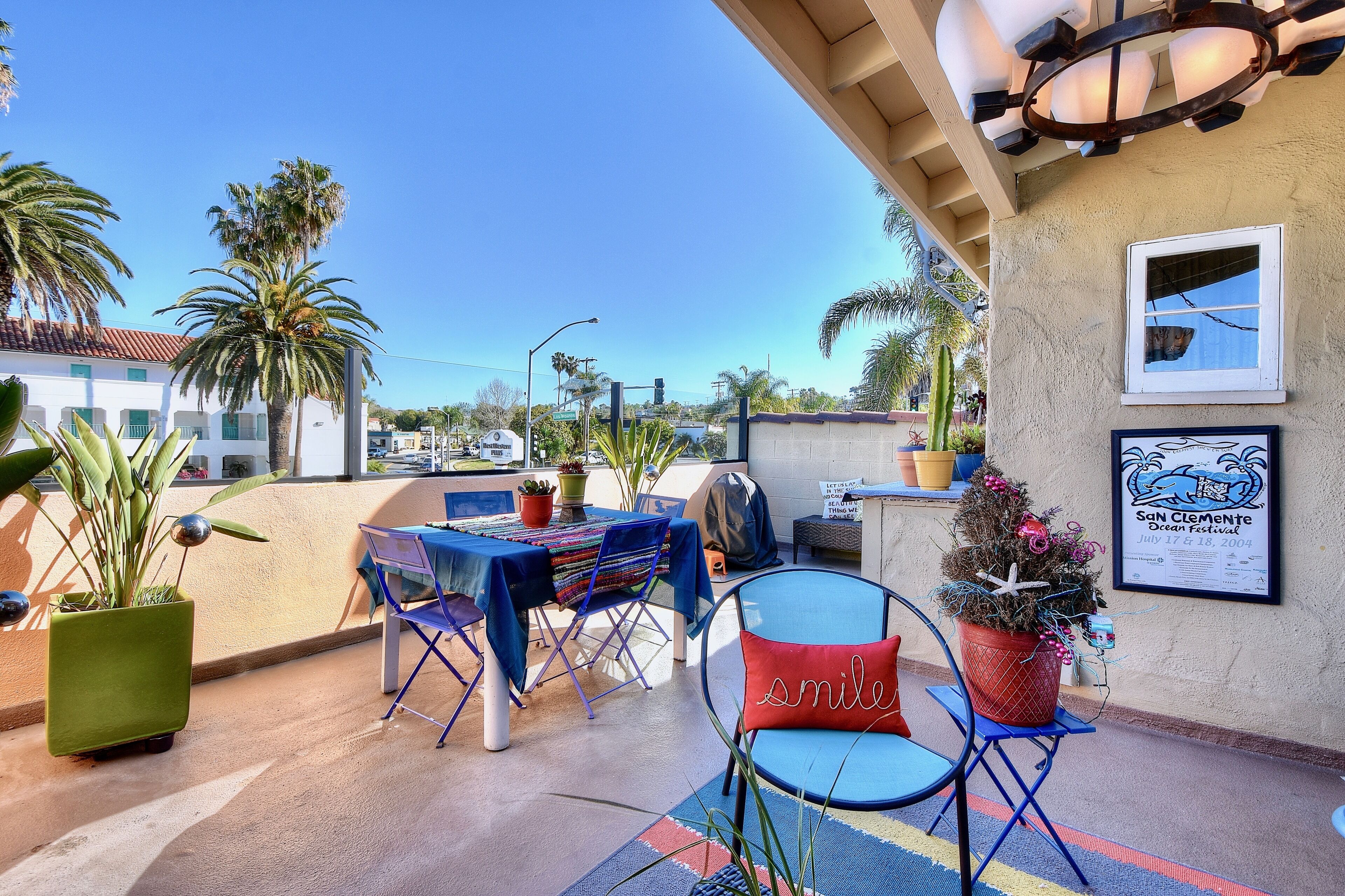 An outdoor patio with tables and chairs, potted plants, and a framed sign.
