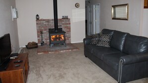 A living room with a brick fireplace, a leather sofa, a television on a wooden stand, and a ceiling fan. - The Decanted Chateau; a two minute drive to Downtown Murphys (Vallecito)