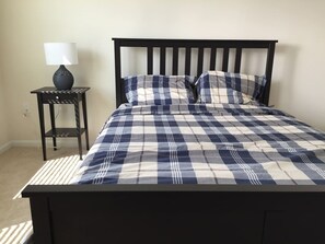 A bed with a checkered bedspread, a bedside table with a lamp, and a power outlet on the wall. - A-Gated Resort-5 miles to Disney-2 FREE Water Park (Osceola County)