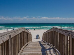 A wooden boardwalk leading to a beach with clear blue water and a few people in the distance. - Perrydise Beautifully Updated Condo Beach Service (Navarre)