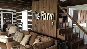Ein gemütliches Wohnzimmer mit einem braunen Sofa, einer Holzwand mit dem Schriftzug "The Farm" und einem Sessel, sowie einer Treppe.