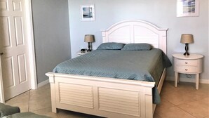 Une chambre à coucher avec un lit, deux tables de chevet, une porte et un tableau accroché au mur.