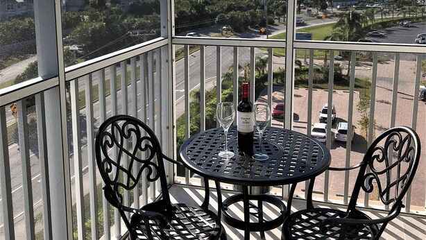 Un balcon avec une table et des chaises, une bouteille de vin et une vue sur l’océan et les bâtiments.