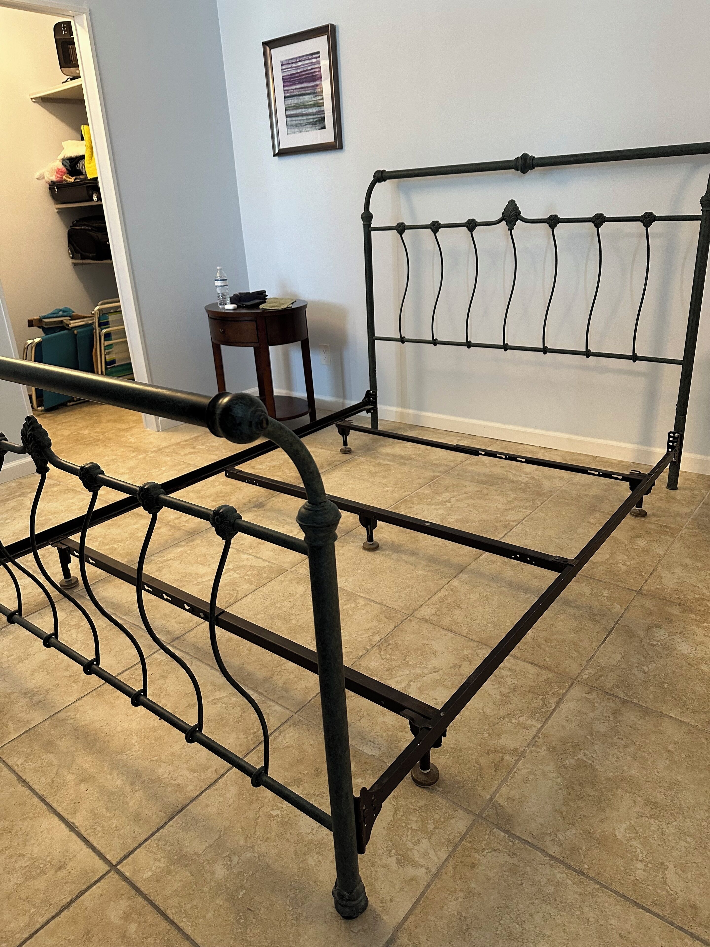 A metal bed frame with a slatted headboard, a small wooden side table, and a tiled floor.