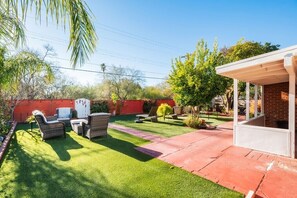 Ein Garten mit Kunstrasen, Gartenmöbeln, einer überdachten Terrasse und einer Ziegelwand.