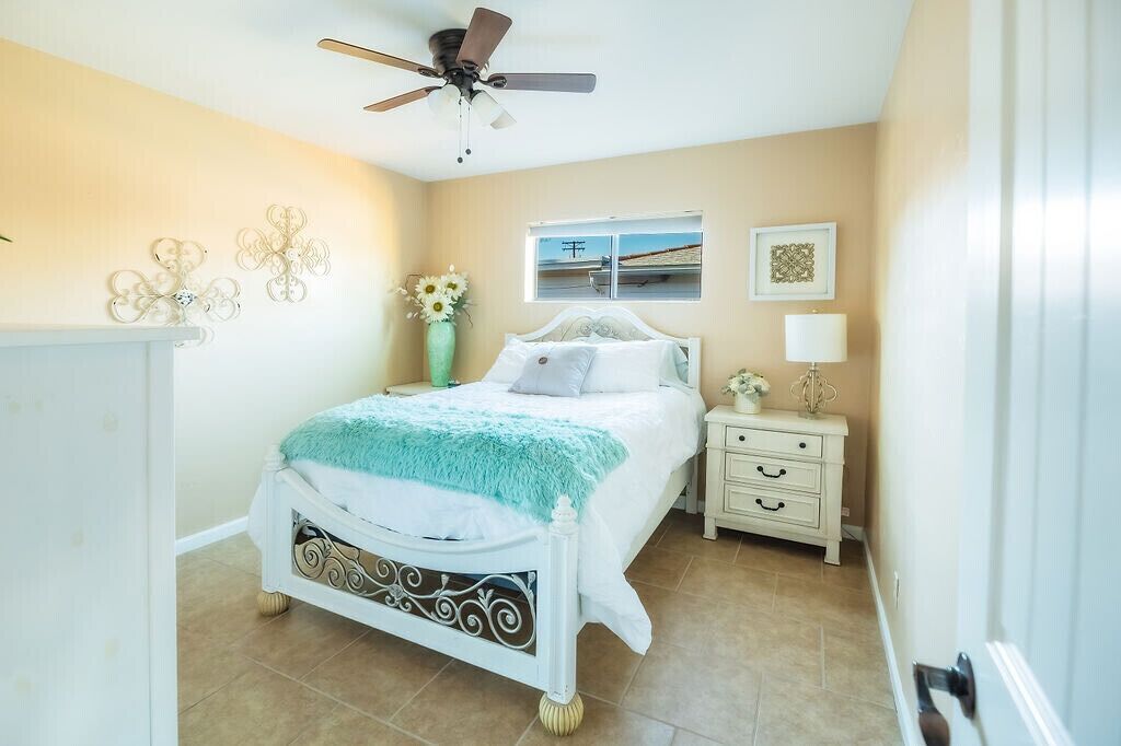 A bedroom with a bed, a nightstand, a lamp, a ceiling fan, and decorative wall art.