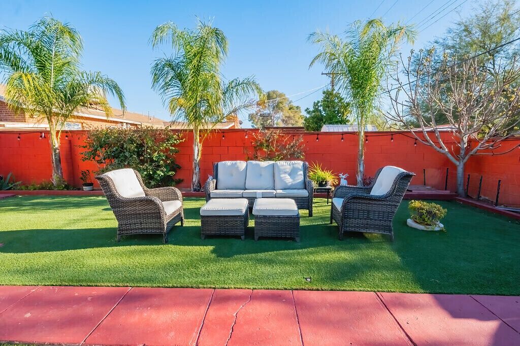A patio with wicker furniture, a red wall, and green grass.