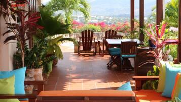A covered patio with wooden furniture, potted plants, and a view of the landscape.