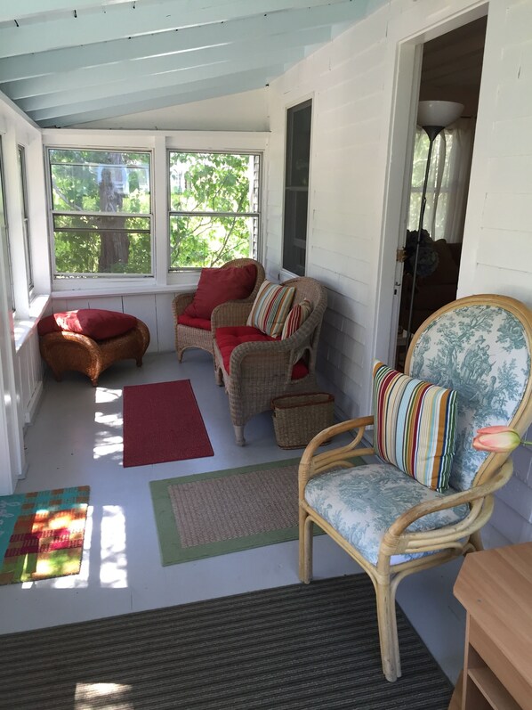 A sunroom with wicker furniture, a red rug, and a view of trees outside.