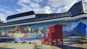 Un mural da la bienvenida a los visitantes a Siesta Key con una escena de playa y una torre de salvavidas.