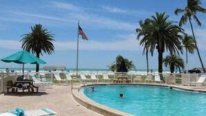 Un área de piscina con sillas de descanso, una bandera y palmeras.