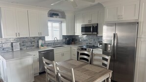 Una cocina moderna con armarios blancos, electrodomésticos de acero inoxidable, una mesa de comedor con sillas y un ventilador de techo.