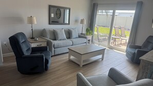 Una sala de estar moderna con un sofá gris, dos sillones, una mesa de centro y un ventanal con vistas al exterior.