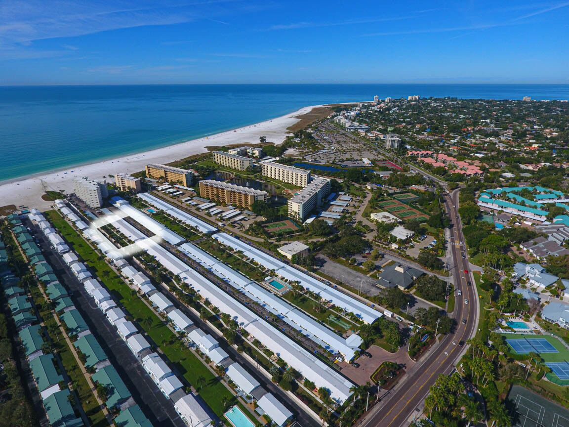 Eine Luftaufnahme eines Küstenhotelareals mit mehreren Gebäuden, einem Strand und einer Straße.