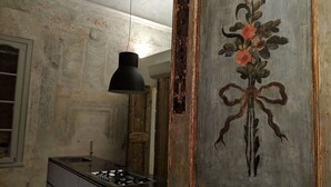 Une pièce comprenant un coin cuisine, un luminaire suspendu et un mur orné d’un tableau représentant des motifs floraux.