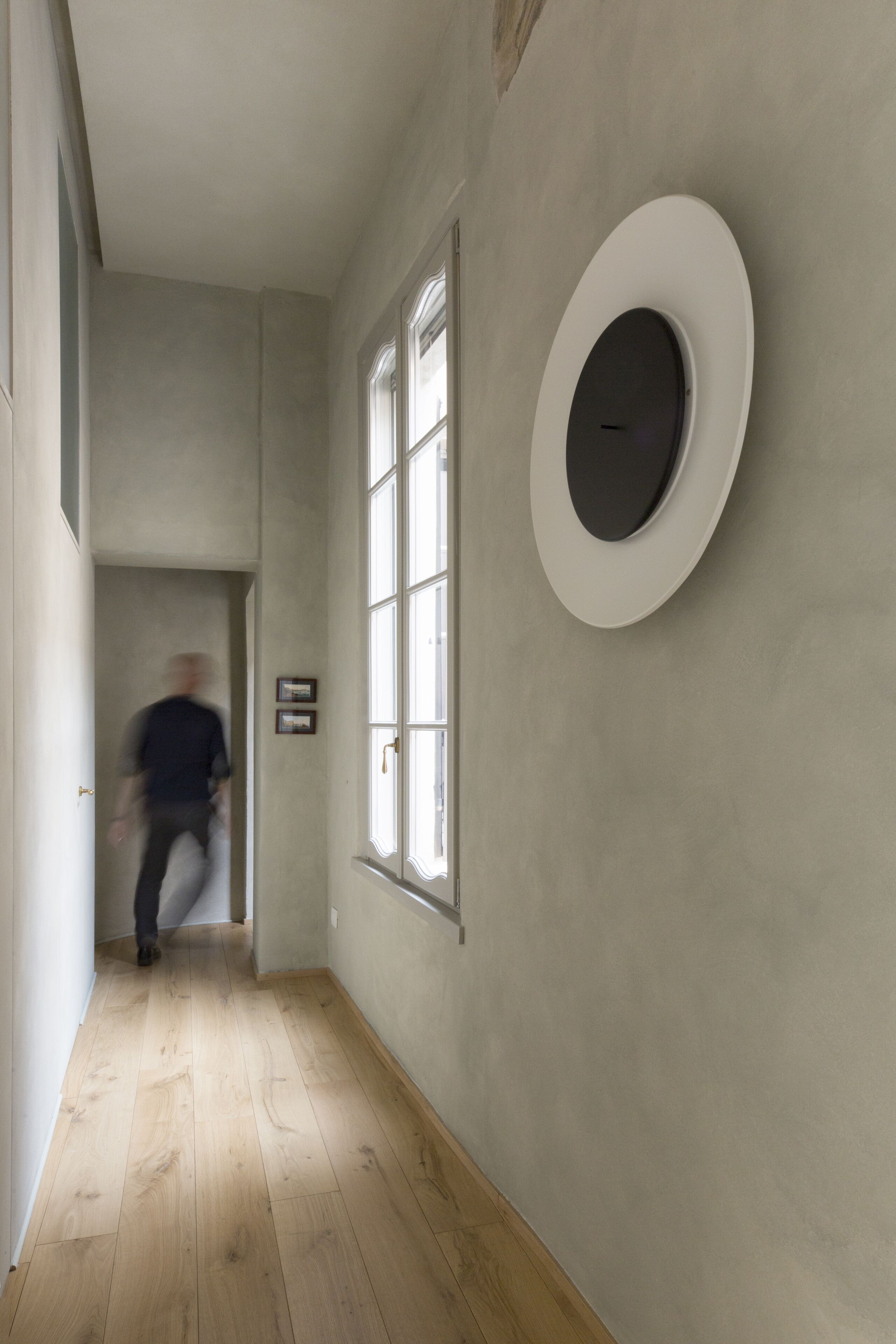 A hallway with wooden flooring, a large window, and a wall-mounted circular object.