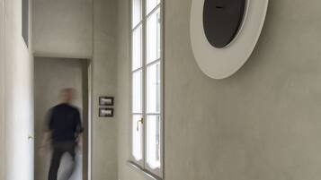 A hallway with wooden flooring, a large window, and a wall-mounted circular object.