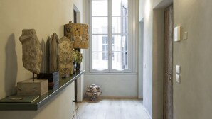 Un couloir avec un plancher en bois, une fenêtre avec des stores et une porte sur le côté droit.
