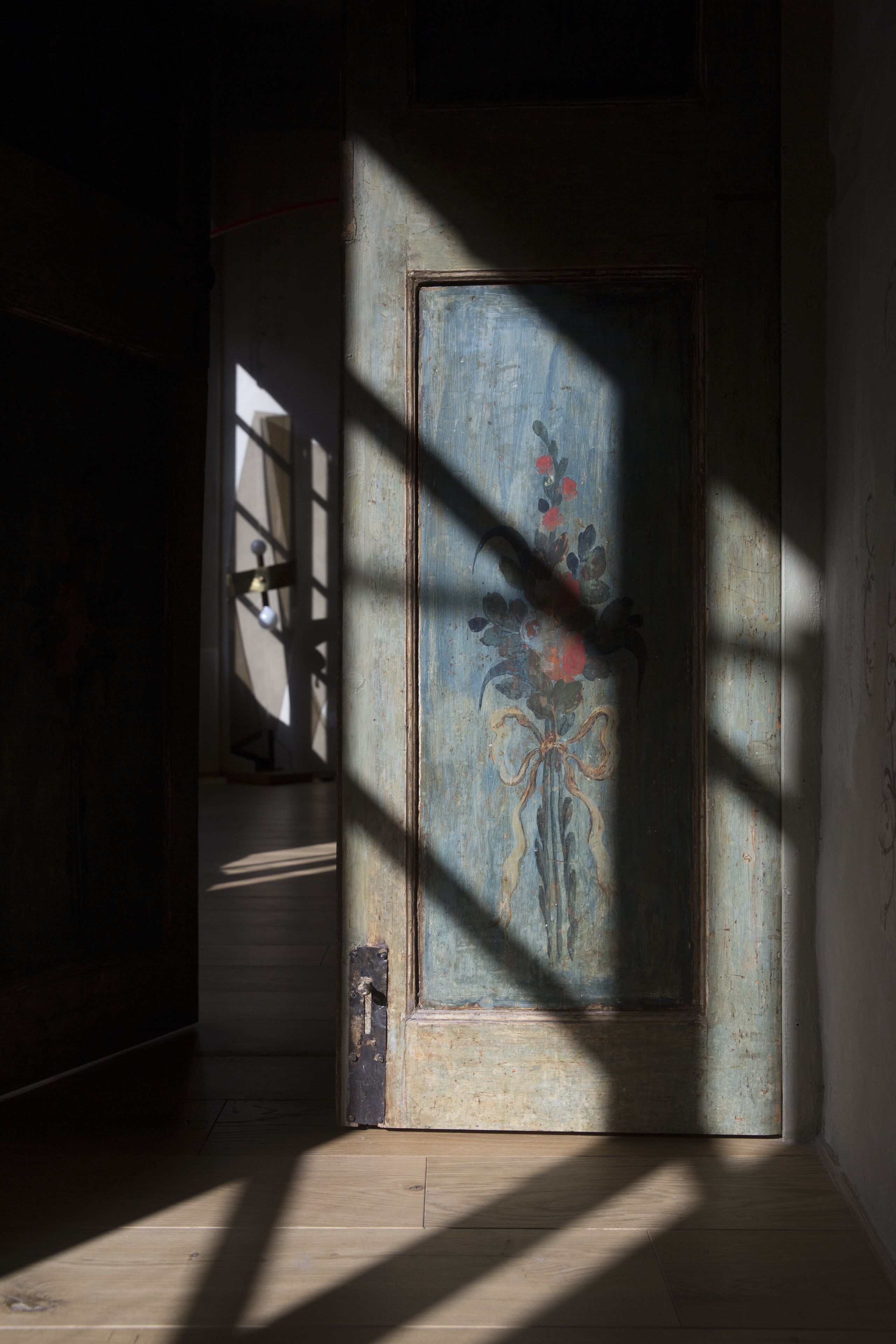 Une pièce dotée d’un plancher en bois, d’une porte ornée de motifs floraux et d’une ombre projetée par une fenêtre.