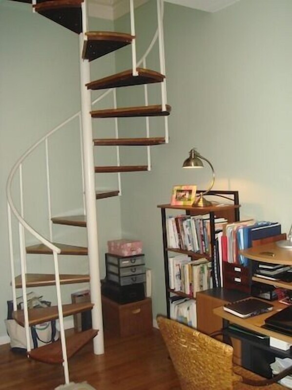 A spiral staircase with wooden steps and white railings, a bookshelf filled with books, a desk with a lamp, and a chair. - Elegant Back Bay Brownstone-Comm Av 1+ Bed - 1 Week Min, beyond 2 wks considered (Boston)