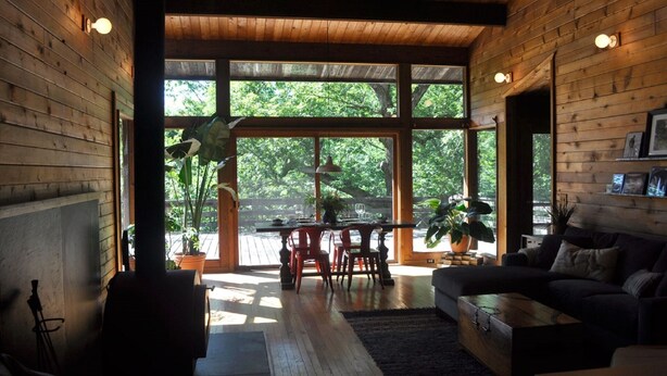 Un salón comedor amplio con techo de madera, ventanas grandes, chimenea y una zona de estar acogedora.