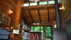 Interior rústico de una cabaña con cocina, comedor y un ventanal grande con vistas a la vegetación.