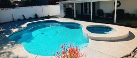 A swimming pool with a hot tub, surrounded by a white fence and a covered patio area.