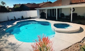 A swimming pool with a hot tub, surrounded by a white fence and a covered patio area.